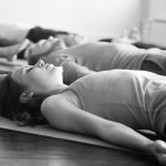 Group of young sporty people practicing yoga lesson with instructor in gym, lying in Dead Body exercise, doing Savasana, Corpse pose, friends relaxing after working out in sport club, studio image